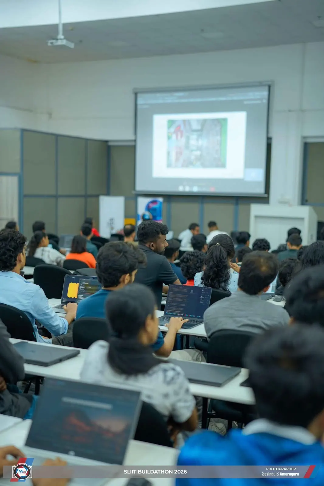 Students working on laptops while a presentation is shown on a projector screen at SLIIT Buildathon 2026