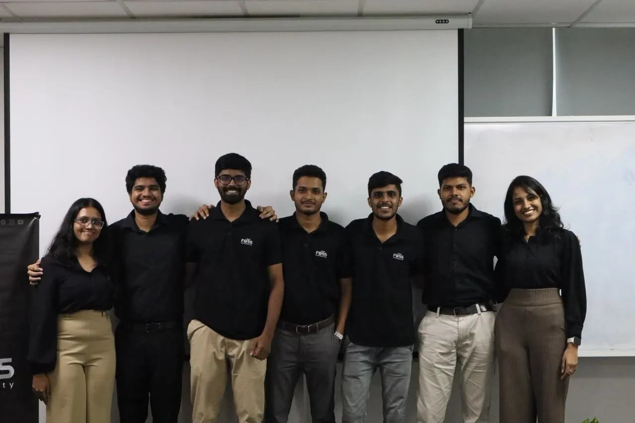 Seven SLIIT FOSS Community team members in black shirts smiling together in front of a projector screen